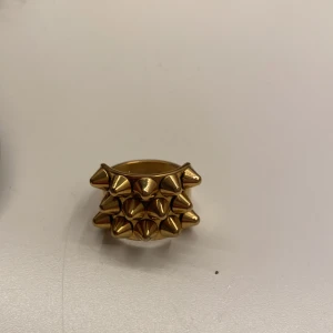 Guldig ring med nitar - Guldig edblad ring med spetsiga nitar. Storlek 17,50, som står på insidan av ringen. Nästan alldrig använd då jag inte använder ringar. Nypris 399kr