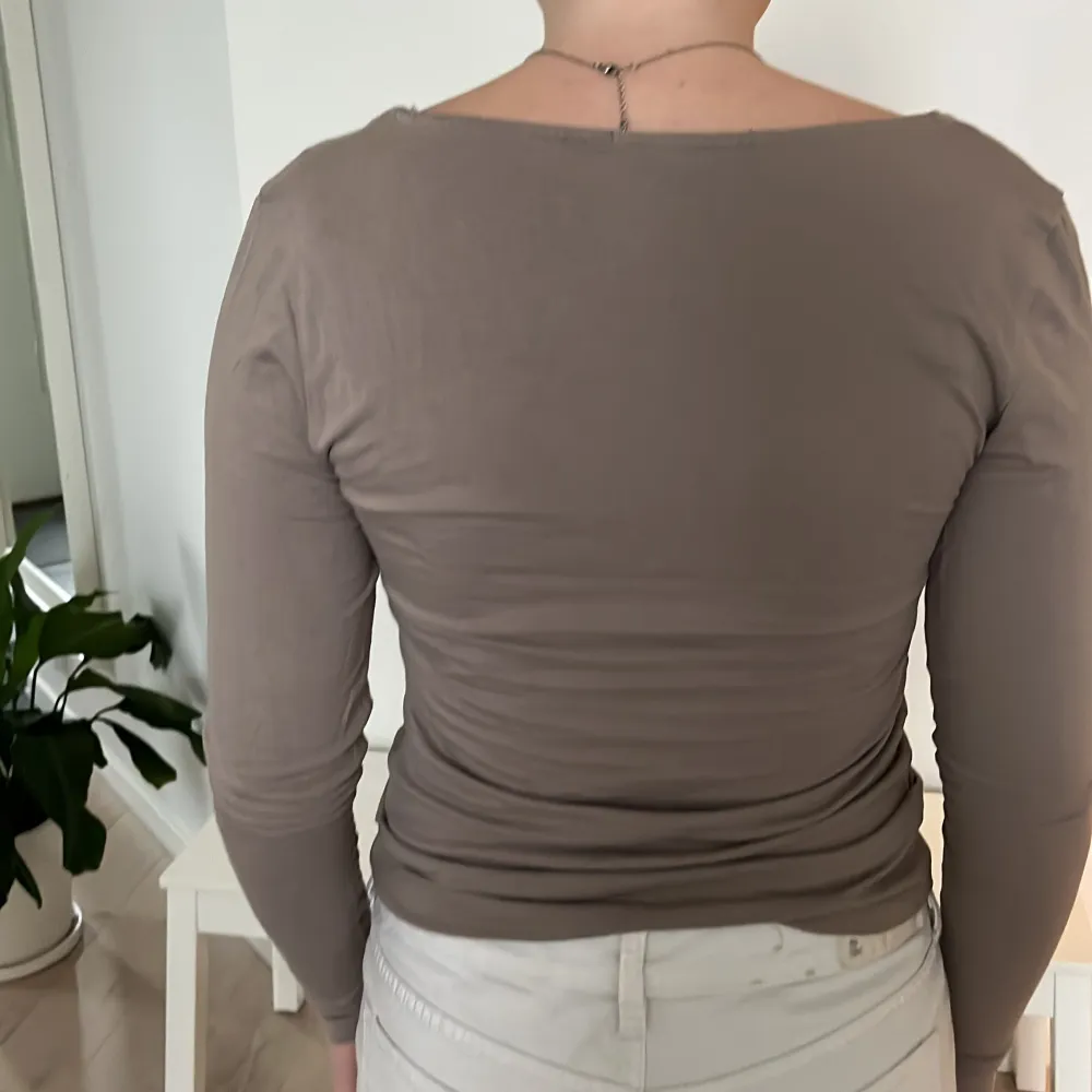 Säljer en stilren beige långärmad topp i mjukt material. Den har en djup rundad halsringning och en tight passform som framhäver figuren. Perfekt för både vardag och festliga tillfällen. Passar bra till jeans eller kjol!. Yläosat.