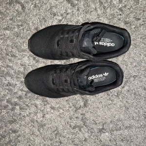 Adidas original ZX Flux  - Säljer ett par svarta Adidas sneakers i mycket bra skick. De har en stilren design med de klassiska tre ränderna på sidan. Perfekta för både vardag och träning. Skorna har snörning och är gjorda i syntetmaterial för en bekväm passform.