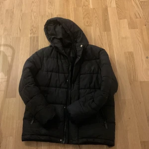 Svart pufferjacka med huva - Säljer en svart pufferjacka i bra skick. Den är perfekt för vintern med sin quiltade design och långa ärmar. Jackan har en praktisk dragkedja och en skön huva för extra värme. Perfekt för kalla dagar! 🖤