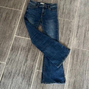 Blå jeans från Lindex - Säljer ett par snygga blå jeans från Lindex i barnstorlek. De har en klassisk bootcut-stil och är i mycket bra skick. Perfekta för både vardag och festliga tillfällen!