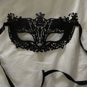 Svart glittrig maskeradmask - Snygg svart maskeradmask som glittrar. Masken har band för att knyta runt huvudet, passar perfekt till maskerad eller annan fest! Oanvänd, köpt på fyndiq