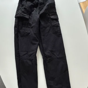 Svarta cargopants Weekday - Säljer ett par svarta cargopants i bra skick. De har flera praktiska fickor och en loose passform som är perfekt för en avslappnad stil. Byxorna är tillverkade i ett slitstarkt material och passar bra till både vardag och äventyr.