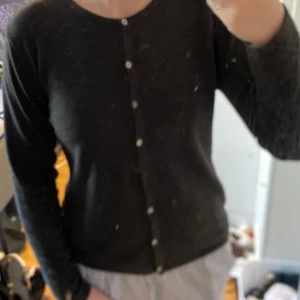 Mörkgrå kofta från Daniels - Säljer en stilren mörkgrå kofta från Daniels i bra skick. Den har långa ärmar och knäpps med små knappar framtill. Perfekt för både vardag och lite finare tillfällen. Passar bra till höst och vinter! Saknar en knapp och har en liten fläk men inget man tänker på när man har koftan på!