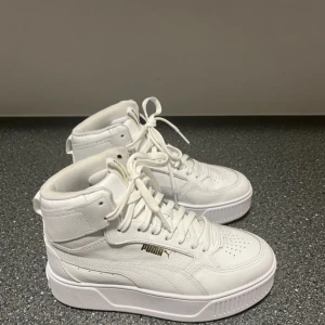 Vita sneakers från Puma - Säljer ett par snygga vita sneakers från Puma i nytt skick. De har en hög modell med snörning. Perfekta för både vardag och fest! 🏆