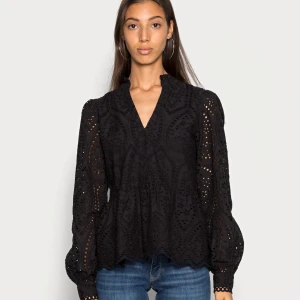 Svart blus med spetsdetaljer - Snygg svart blus med v-ringning och spetsdetaljer. Blusen har långa ärmar och ett fint mönster som ger en elegant touch. Perfekt för både vardag och fest!