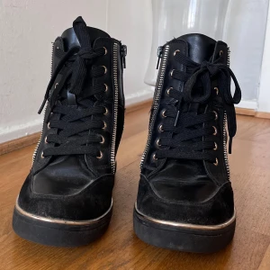 Svarta sneakers  - Svarta sneakers med 7 cm klack och gulddekor, gott skick.