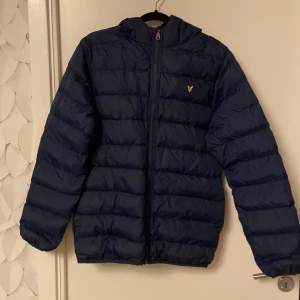 Mörkblå light puffer  från Lyle & Scott - Säljer en snygg mörkblå jacka från Lyle & Scott i storlek 12/13 år. Jackan har en quiltad design med dragkedja.  Perfekt för höst och vår,  håller dig varm och stilren. Kostar ny 1199 kr på Kids Brandstore.