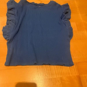 Blå ribbad topp med volangdetaljer - FINNS FLER VOLANG-TRÖJOR PÅ MIN PROFIL! Tröjan är 11-12 / 152 men passar mig som är XXS-S! Säljer en superfin blå ribbad topp med volangdetaljer på ärmarna. Perfekt för både vardag och fest! Toppen har en normal passform  Passar perfekt till jeans eller kjol för en snygg look. 💙