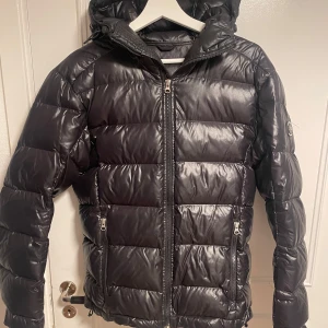 J Lindeberg dunjacka - En glansig j lindeberg dunjacka i fint skick, alla dragkedjor fungerar bra, inga hål i jackan eller slitningar. Det enda är att tagen har spruckit på insidan men det är inget som påverkar jackan eller syns när man har den på sig.