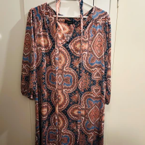 Mönstrad klänning från AA Studio - Säljer en färgglad och mönstrad klänning från AA Studio. Den har trekvartsärmar och ett bohemiskt mönster i blått, rosa och orange. Perfekt för vår och sommar! Klänningen är i storlek 14 och har en bekväm passform.