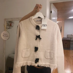 Zara Kofta - Jätte gullig biege,vit zara kofta med svarta rosseter!Köpt i Paris och är verkligen så fin och exklusiv!!! Storlek M men passar mig som är xs/s !skulle inte säga att de är en storlek M 49euro = 580kr (helt ny och oanvänd) 