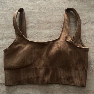 Brun ribbad och vit oneshoulder träningstoppen/bh - Säljer två snygga träningstoppar! En brun ribbad topp med breda axelband och en vit oneshoulder topp. Säljer båda i ett paketpris