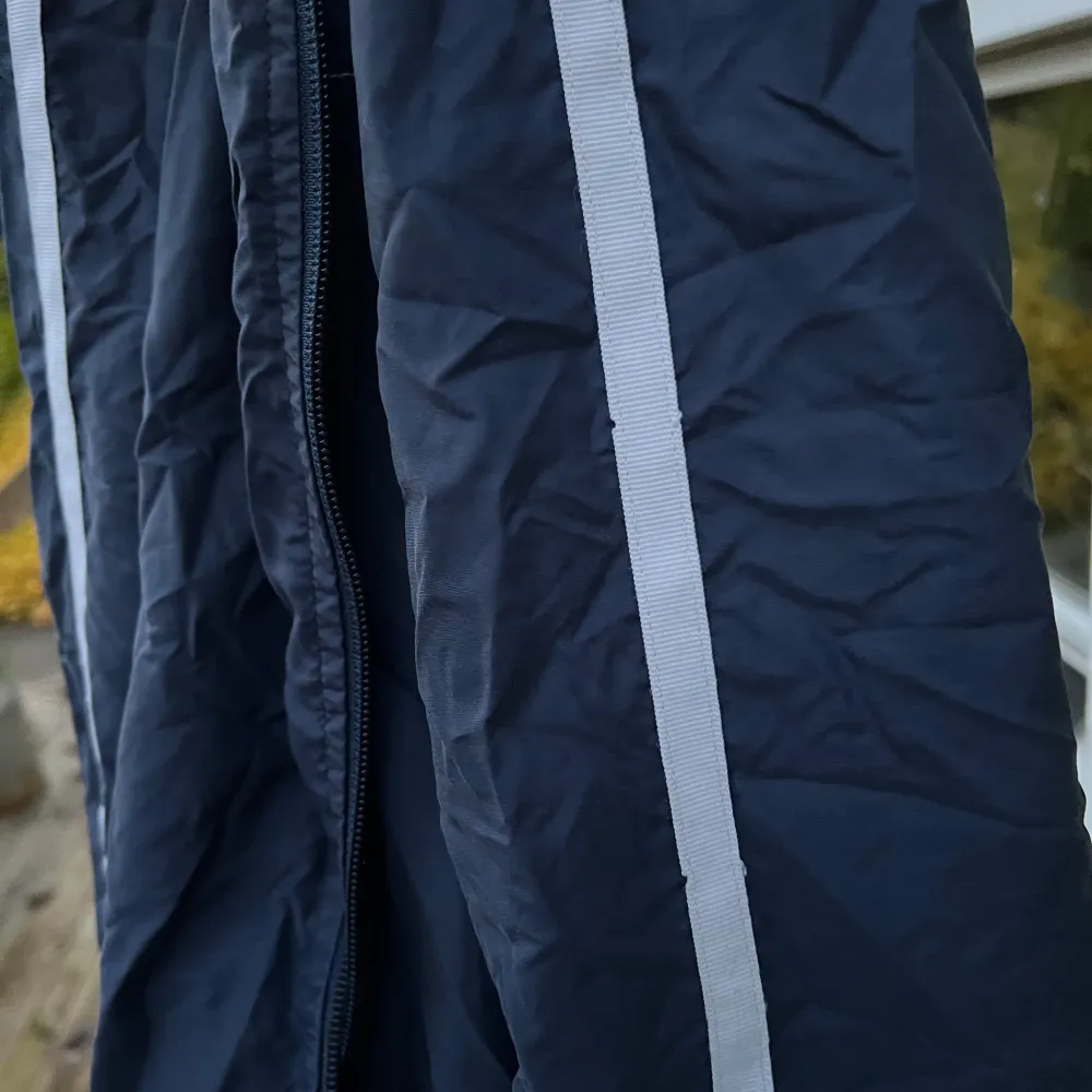 Säljer en blå tunnare jacka från Nike. Tyvärr är den lite skrynklig just nu då den legat i en påse ett tag. Jackan har en dragkedja framtill och en vit rand längs ärmarna. Med en normal passform och långärmade ärmar. Den har sina skavanker och därav säljs den billigt, bifogat bilder på skavankerna.. Takit.