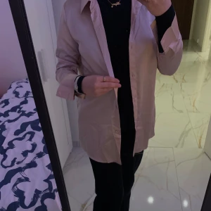 Ljusrosa silkeslik skjorta - Säljer en stilren beige skjorta i normal passform. Skjortan har långa ärmar och klassisk krage, perfekt för både vardag och fest. Den är i ett mjukt och bekvämt material som ger en elegant look. Passar bra till både jeans och kostymbyxor.