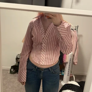 Rosa och vit randig skjorta - Säljer en snygg rosa och vit randig skjorta i storlek L. Skjortan har långa ärmar och knappar framtill. Perfekt för både vardag och fest! 💖
