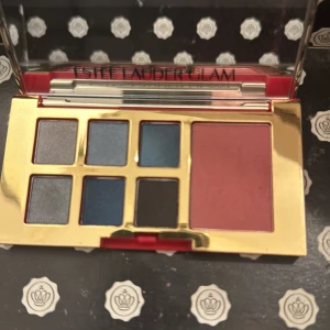 Ögonskuggspalett från Estée Lauder - Snygg ögonskuggspalett från Estée Lauder med sex olika nyanser i blått, grått och svart samt en rouge i en varm rosa ton. Paletten har en lyxig guldig design med ett mönstrat lock. Perfekt för både vardag och fest!