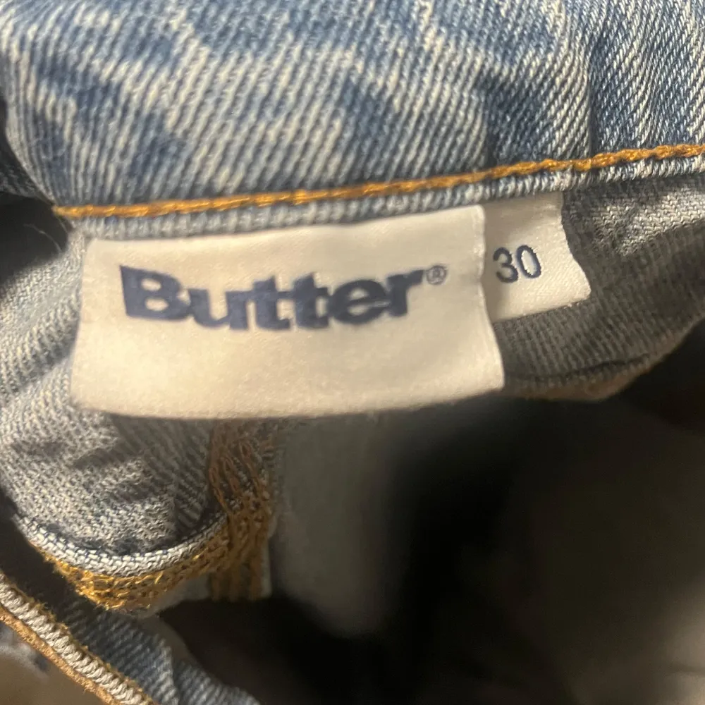 Säljer ett par snygga jeansshorts från Butter i storlek 30. De är i en klassisk blå denimfärg med coola detaljer som en broderad logga på bakfickan. Shortsen har en normal passform och är perfekta för sommaren. De har både knappar och en snörning i midjan för bästa passform. Perfekta för en avslappnad stil!. Shorts.