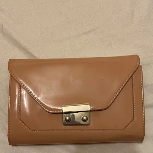 Beige kuvertväska med metallås - Säljer en stilren rosa  kuvertväska i syntetmaterial med ett snyggt metallås framtill. Väskan har flera fack inuti, inklusive ett med dragkedja, perfekt för att organisera dina saker. Passar både till vardags och festliga tillfällen. 💼✨säljs för 40