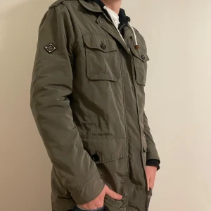 Olivgrön fieldjacket från J.Lindeberg  - Säljer en olivgrön fieldjacket från j.lindeberg i mycket bra skick. Jackan har flera fickor med knappar. Nypris: 2900kr. Modellen är 183cm lång. Kontakta mig för mer frågor, pris kan diskuteras!