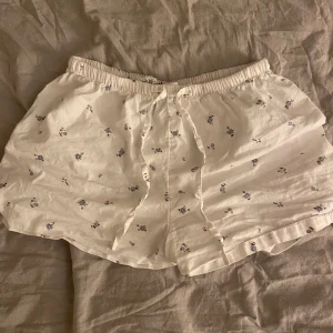 Low waist shorts med blom tryck i vit  - Ursinnigt söta shorts som liknar Brandy Melville, perfekt att ha hemma eller som pyjamas! I bra kondition som använts ett par gånger. Dessa är i storlek XS och är i sann storlek! Passar mig i storlek S men liteee tajt i midjan. 💓🎧 