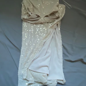 Glittrig klänning  - Lång tight glittrig klänning i färgen beige. Perfekt för bal, bröllop eller utekvällar med vänner! Klänningen har dessutom en snygg öppning vid midjan som verkligen lyfter hela looken! 🪩⭐️