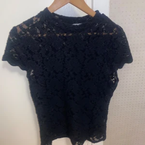 Svart spetsblus - Säljer en elegant svart spetsblus i mycket bra skick. Den har korta ärmar och ett jättefint  spetsmönster. Perfekt för både fest och vardag. Storlek L men passar mig superbra som har S/M vanligtvis. Passar bra till jeans eller kjol🖤