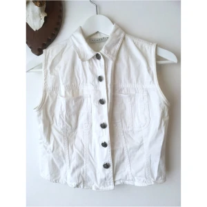 Vit kort jeansväst, 36 S, cropped, croppad, vintage, retro, denim, jeans, knappar - Vit väst i tunnare denim, figurnära kort modell. Lätt gulnad på insidan av nacken. Storlek (EU): 36 (något liten, passar XS/S), Bröstvidd: 43 cm, Axelbredd: 32 cm, Längd fram från axeln: 43 cm