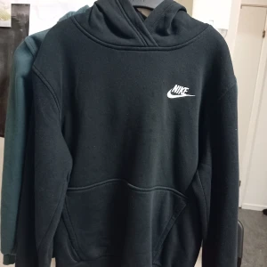 Svart hoodie från Nike - Säljer en klassisk svart hoodie från Nike i storlek M (137-147). Den är superbekväm och perfekt för både vardag och träning. Hoodien har en känguruficka och det ikoniska Nike-loggan på bröstet. Perfekt för höst och vinter!