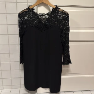 Svart spetsklänning från Zara Basic - Elegant svart klänning från Zara Basic med vackra spetsdetaljer på överdelen och ärmarna. Klänningen har en normal passform och trekvartsärmar, perfekt för en stilren look. Tillverkad i ett mjukt och bekvämt material.