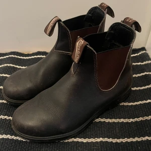 Bruna boots från Blundstone - Säljer ett par klassiska mörkbruna boots från Blundstone. De har en robust design med elastiska paneler på sidorna och dragflikar för enkel påtagning. Perfekta för både stad och natur.