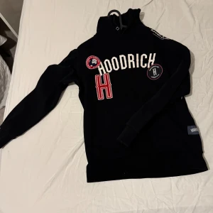 Svart hoodie från Hoodrich - Säljer en svart hoodie från Hoodrich med vita och röda detaljer. Tröjan har långa ärmar och en hög krage med snörning. Perfekt för en avslappnad stil. Sitter riktigt bra på kroppen, pris kan diskuteras.
