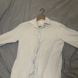 Randig skjorta från Massimo Dutti - Snygg och stilren skjorta från Massimo Dutti i blå och vit randigt mönster. Skjortan har långa ärmar och knappar framtill. Perfekt för en klassisk look. Perfekt för en middag eller nu när sommar vädret börja smyga in igen! 