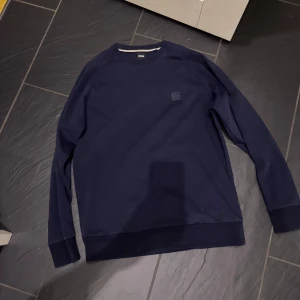 Svart sweatshirt från BOSS - Snygg svart sweatshirt från BOSS med rund hals och diskret logotyp på bröstet. Perfekt för en stilren och avslappnad look. Tröjan har långa ärmar och är tillverkad i ett mjukt material för extra komfort.