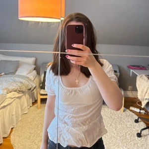 Vit blus från XOXO - Säljer en söt vit blus från XOXO med korta puffärmar och en elastisk halsringning. Blusen har en lätt volangdetalj vid nederkanten som ger en romantisk touch. Perfekt för varma dagar!