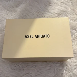 Vita sneakers från Axel Arigato - Snygga vita sneakers från Axel Arigato med en stilren design. Skorna har en tjock sula och är tillverkade i skinn. Perfekta för en trendig look!!❤️plus man får med lådan!!