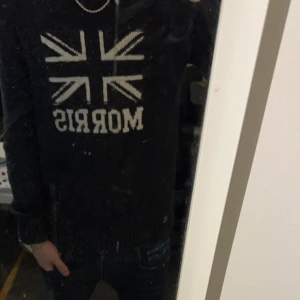 mörkblå tröja från Morris - Säljer en mörkblå tröja från Morris med ett stort tryck av Union Jack-flaggan och texten 'Morris' på framsidan. Tröjan har långa ärmar och en klassisk passform. Perfekt för en stilren och avslappnad look. Storlek M bra skick