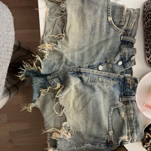 Blå jeansshorts från Zara - Snygga blå lågmidjade jeansshorts från Zara med slitna detaljer och fransar.