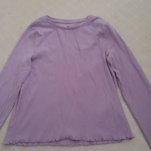 Lila ribbad tröja från H&M - Säljer en söt lila ribbad tröja från H&M. Tröjan har långa ärmar och en enkel design med vågiga kanter vid ärmslut och nederkant. Perfekt för en avslappnad stil. 💜