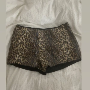 Leopardmönstrade shorts med paljetter - Snygga leopardmönstrade shorts med glittrande paljetter. Perfekta för att sticka ut på festen. De har en tight passform och är gjorda i ett syntetmaterial som ger en glansig look.