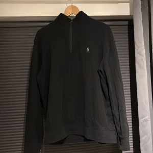 Svart tröja från Ralph Lauren - Säljer en stilren svart tröja från Ralph Lauren med halv dragkedja och det klassiska broderade logotypen på bröstet. Perfekt för en avslappnad men ändå elegant look. Skick 8/10 och inga större tecken på användning.