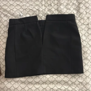 Svart kortkjol - Snygg svart kortkjol med en stilren design. Kjolen har en dragkedja baktill och diskreta fickor. Perfekt för en elegant look.