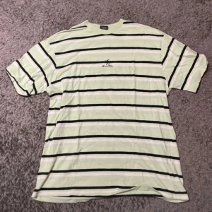 Randig t-shirt från Sweet SKTBS - Säljer en randig t-shirt från Sweet SKTBS i ljusgrön och svart. T-shirten är kortärmad och tillverkad i 100% bomull, vilket gör den bekväm och lätt att bära. Perfekt för en avslappnad stil.