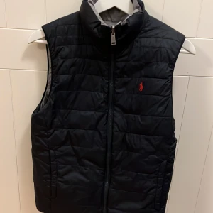 Blå och grå quiltad väst från Ralph Lauren - Snygg quiltad väst från Ralph Lauren i blått och grått. Västen har två olika sidor storlek 160-165 cm