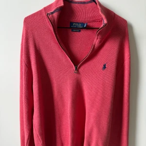 Rosa tröja med dragkedja från Ralph Lauren - Snygg rosa tröja från Ralph Lauren med en liten blå logga på bröstet. Tröjan har en dragkedja vid halsen och långa ärmar. Perfekt för en stilren look.