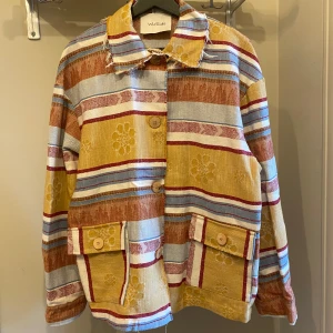 Färgglad randig vårjacka  - Oanvänd , tillverkad i Italien 🇮🇹                      Unik tunn jacka/overshirt med färgglatt randigt mönster i gult, blått, rött och beige. Jackan har stora knappar framtill och praktiska fickor. 