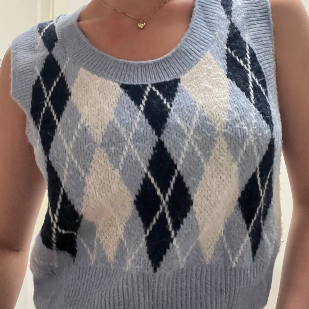 Snygg blå stickad väst från Monki med ett klassiskt argyle-mönster i svart och vitt. Perfekt för lager-på-lager-stil och ger en trendig touch till din outfit.. Neuleet.