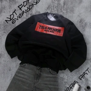 True Religion Sweatshirt  - Säljer en svart sweatshirt från True Religion med en röd och svart logga på bröstet. Perfekt för en avslappnad stil. Nypris 1000kr , Storlek L