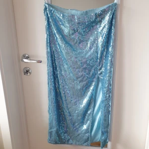 Blå glittrig kjol från Gina Tricot - Snygg blå glittrig kjol från Gina Tricot med en elegant slits. Perfekt för att sticka ut med sin skimrande paljettfinish. Kjolen har en tight passform och är i en längre modell. Inköpt för 499kr.                                      https://www.ginatricot.com/se/klader/kjolar/gloria-sequins-skirt-182155000