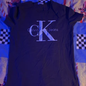Svart t-shirt från Calvin Klein Jeans - Säljer en svart t-shirt från Calvin Klein Jeans med det ikoniska CK-logotypen tryckt i vitt på framsidan. T-shirten har en klassisk rund hals och korta ärmar. Perfekt för en stilren och avslappnad look.